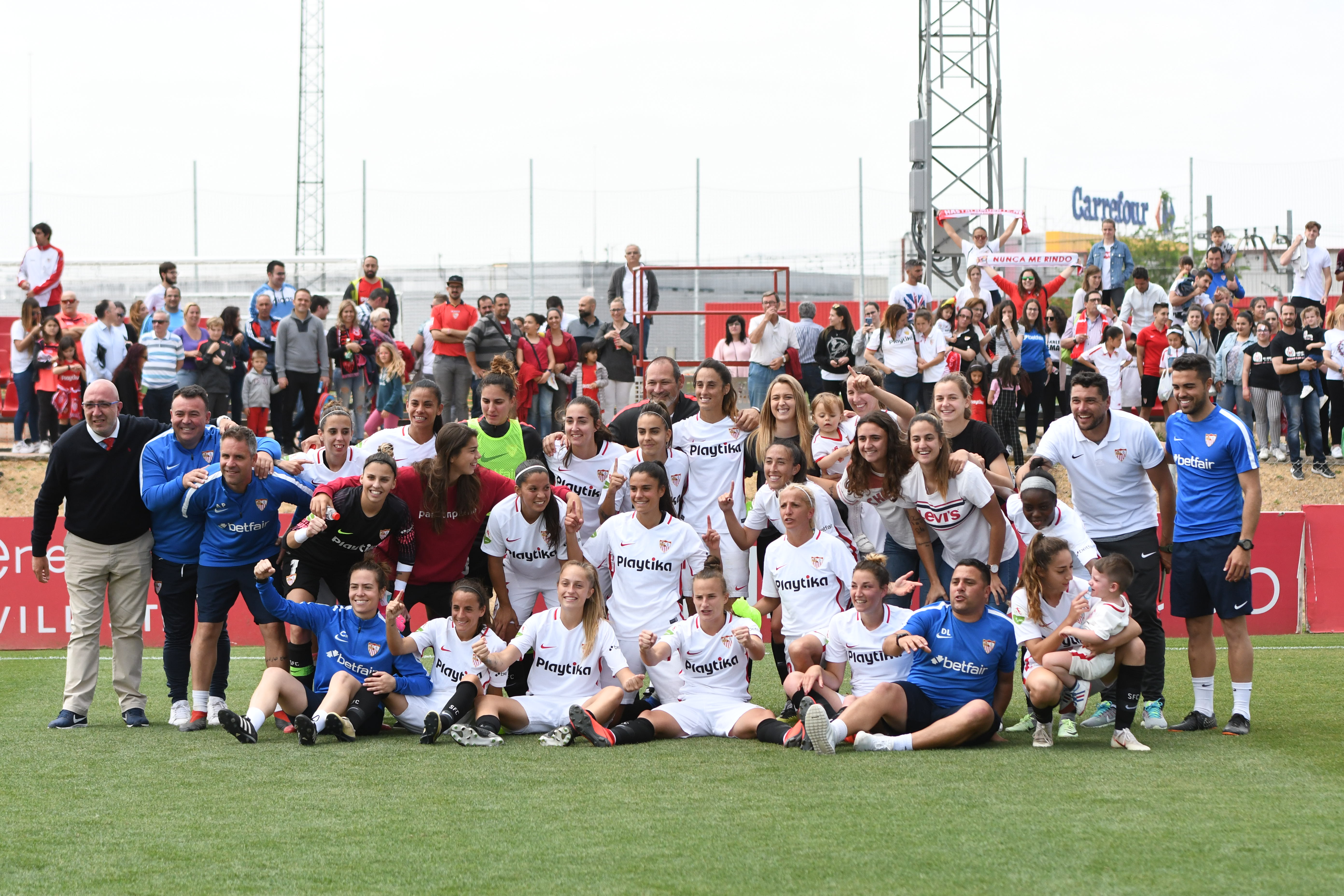 El primer equipo femenino del Sevilla FC posa junto a los aficionados sobre el césped del campo 4 de la ciudad deportiva tras confirmar la permanencia en la Liga Iberdrola